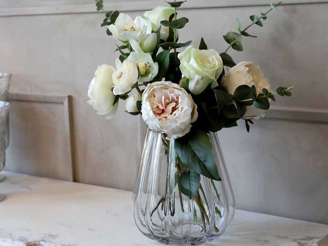 Ein Strauß weißer Rosen und Grünpflanzen in einer klaren Glasvase auf einer Marmorarbeitsplatte.