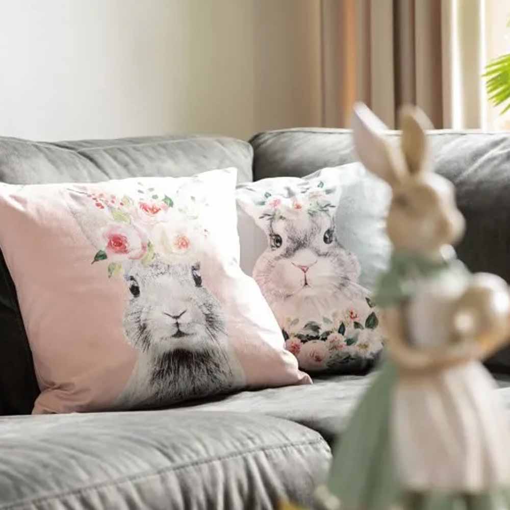 Zwei dekorative Kissen mit Clayre & Eef – Kissenbezug Hase mit Blumen Samt rosa Designs auf einem Sofa.