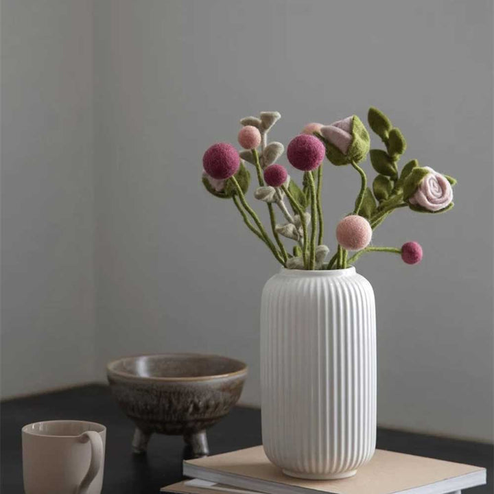 Eine weiße Keramikvase mit Kunstblumen von Gry & Sif – Rose Filz auf einem Tisch, dazu eine kleine Tasse und eine strukturierte Schale.