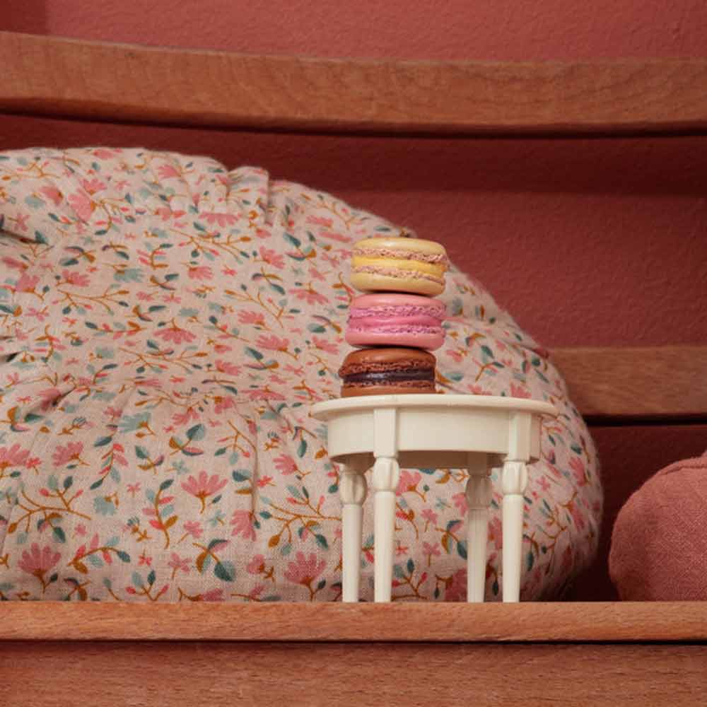 Maileg – Puppenhaus Tisch klein mit bunten Macarons gestapelt auf einem Blumenkissen vor rosa Hintergrund.