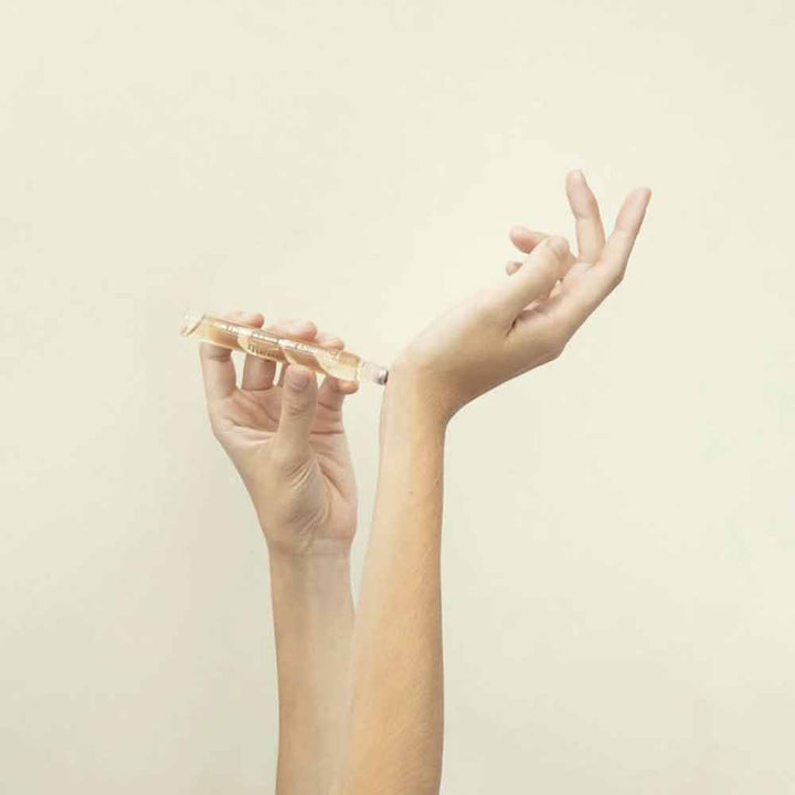 Eine Hand hält einen Panier des Sens – Eau de Toilette Roll-on Rosengeranie 10 ml, die andere Hand streckt sich vor einem beigen Hintergrund nach oben.