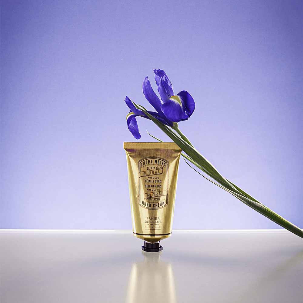 Eine einzelne violette Iris ruht auf einem Panier des Sens - Handcreme Irisblüttenblätter vor blauem Hintergrund.