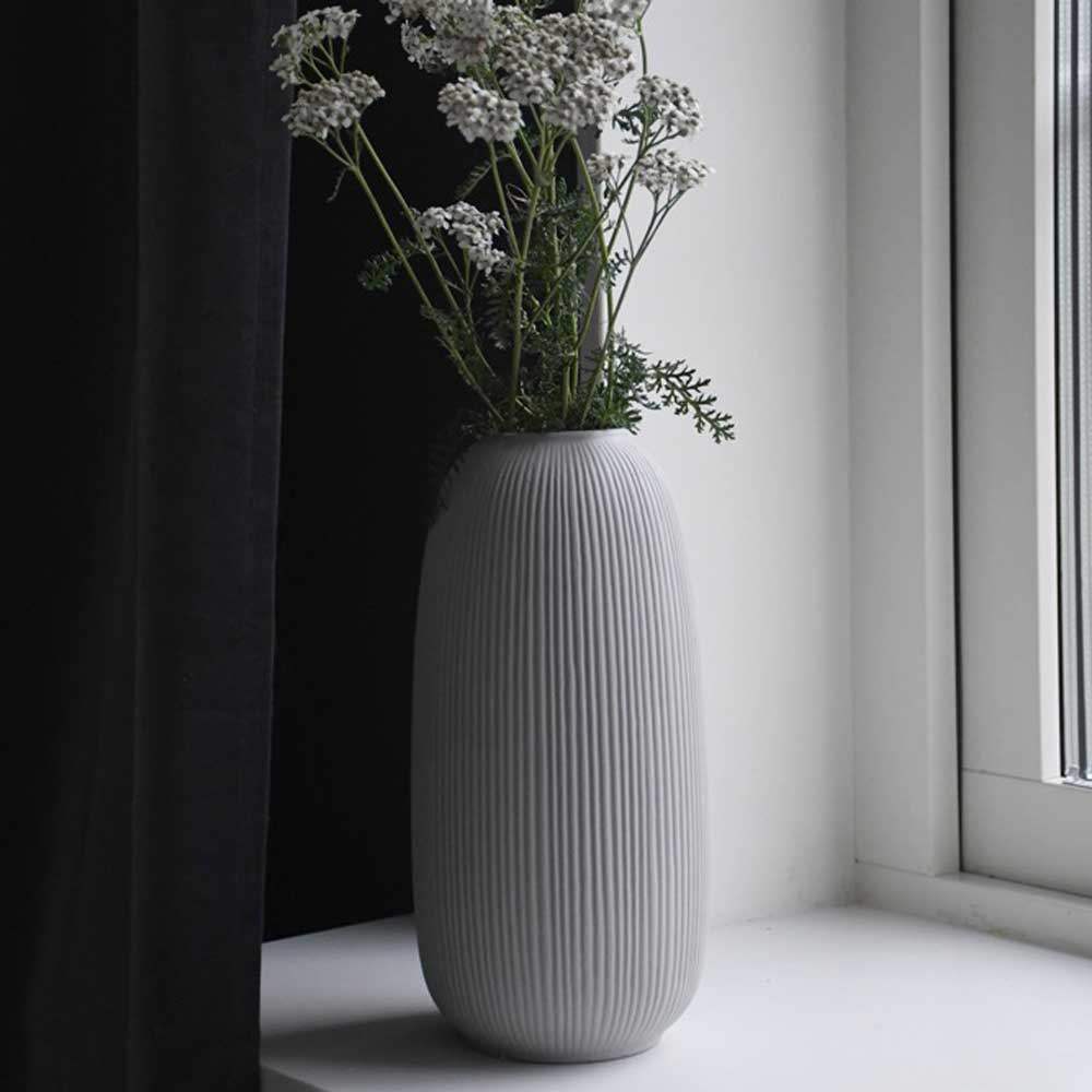 Hellgraue gerillte Åby mit weißen Blüten neben einem dunklen Vorhang am Fenster