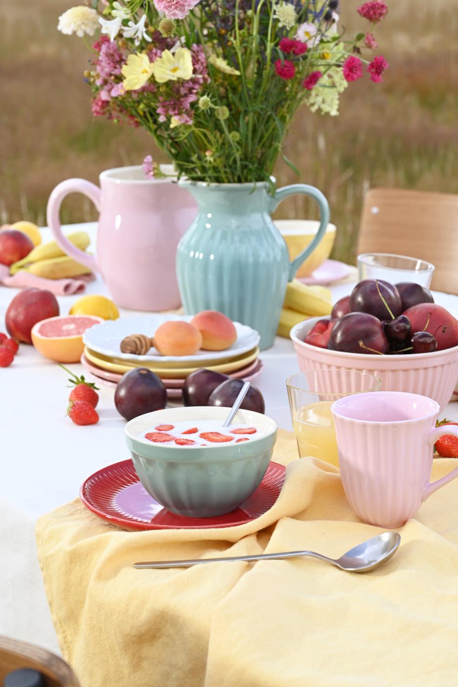 Ein farbenfrohes Picknick im Freien mit einer Schüssel Joghurt, frischen Früchten und einer Vase mit Wildblumen auf einer mit Stoff bedeckten Ib Laursen - Kanne 2,5 Liter Mynte.