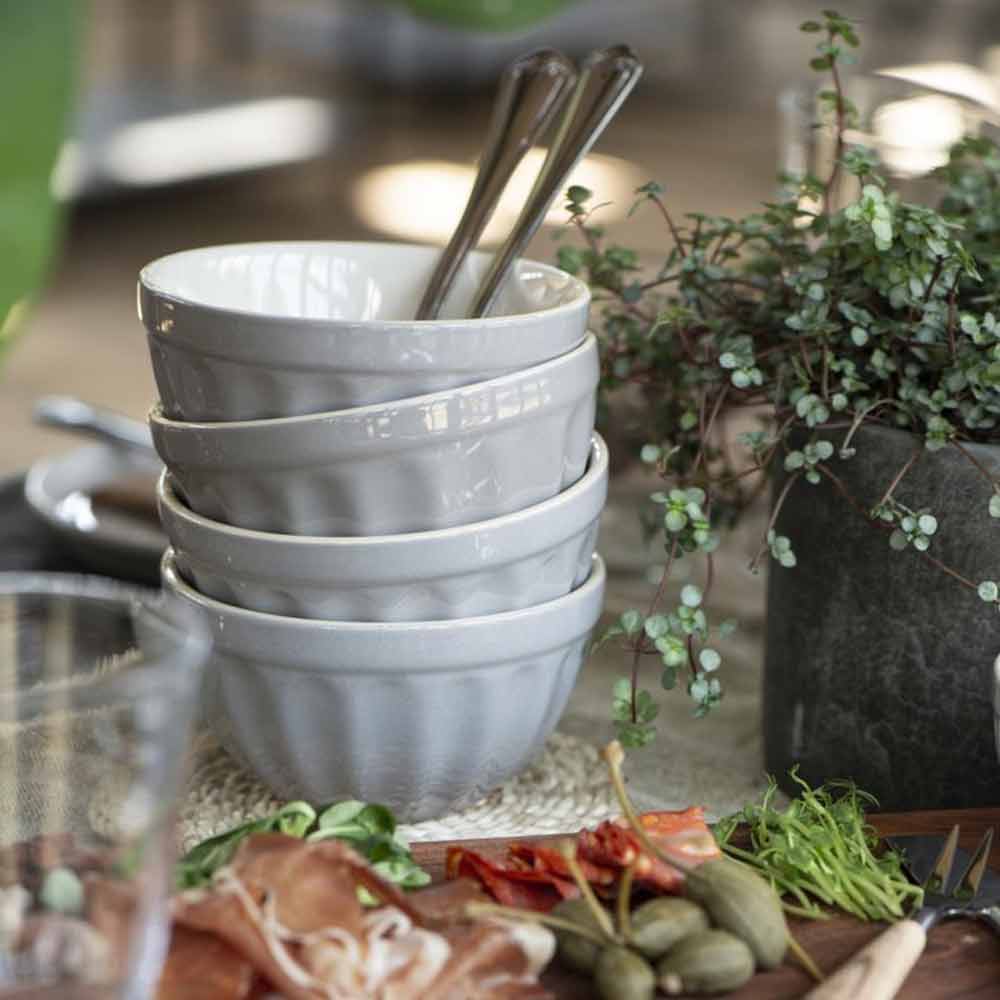 Stapel von Ib Laursen - Müslischale Mynte-Schüsseln mit silbernen Löffeln darin, umgeben von einer Wurstplatte mit Fleisch, Oliven und anderen Beilagen, neben einer Topfpflanze.