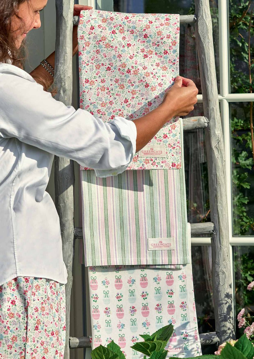 Eine Frau legt weiße Handtücher von GreenGate - Elsie Geschirrtuch auf eine Leiter in einem Garten.