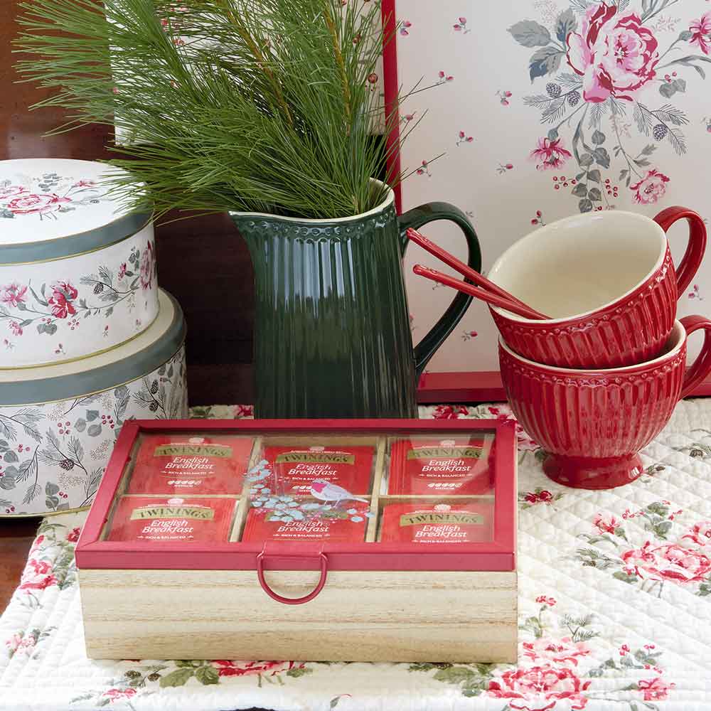 Ein GreenGate - Leonora Tischset, weiß gesteppt mit einer roten Kanne, Schachteln mit Twinings-Tee und einem floralen Hintergrund auf einer gesteppten Oberfläche.