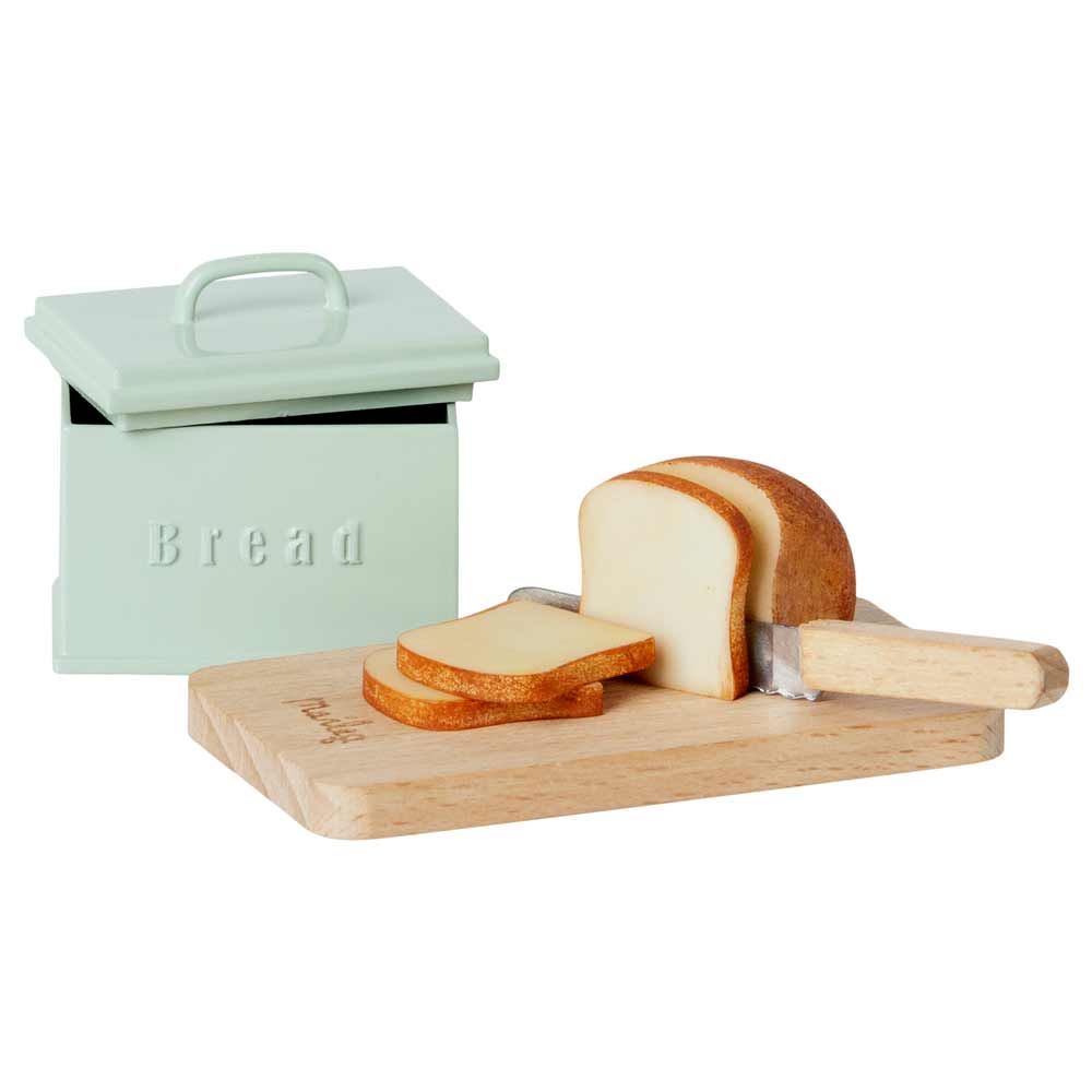 Eine Maileg - Puppenhaus Brotbox neben einem Holzschneidebrett mit einem Laib geschnittenem Brot und einem Brotmesser.
