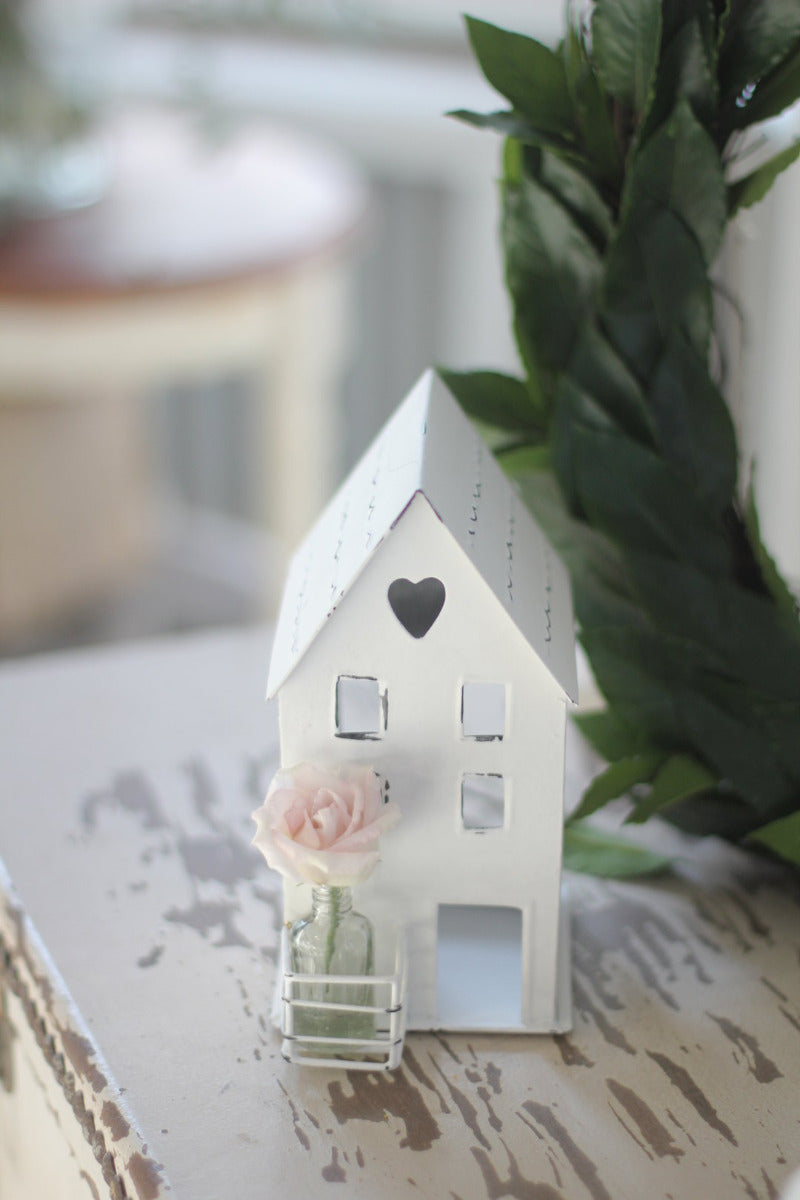 Ein kleines VL Home - Metallhaus weiß Herz Fenster mit Glasflasche auf einem Tisch mit einer Blume darin.