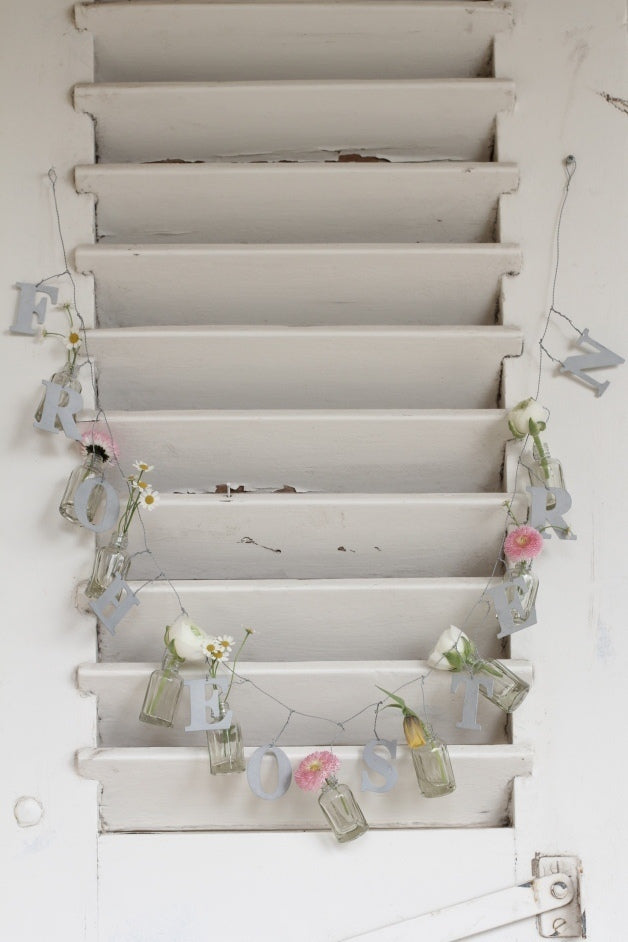 Weiße Treppe dekoriert mit Vl Home - Girlande Frohe Ostern und Blumen in Gläsern.