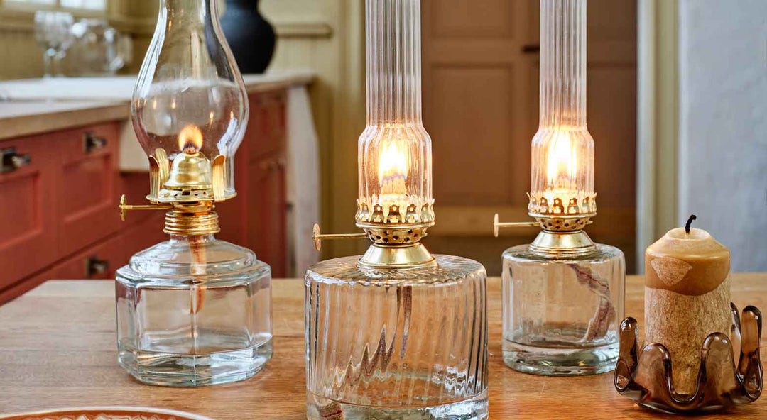Drei Öllampen mit brennenden Flammen auf einem Holztisch in einer warm beleuchteten Küche mit rustikalem Dekor.