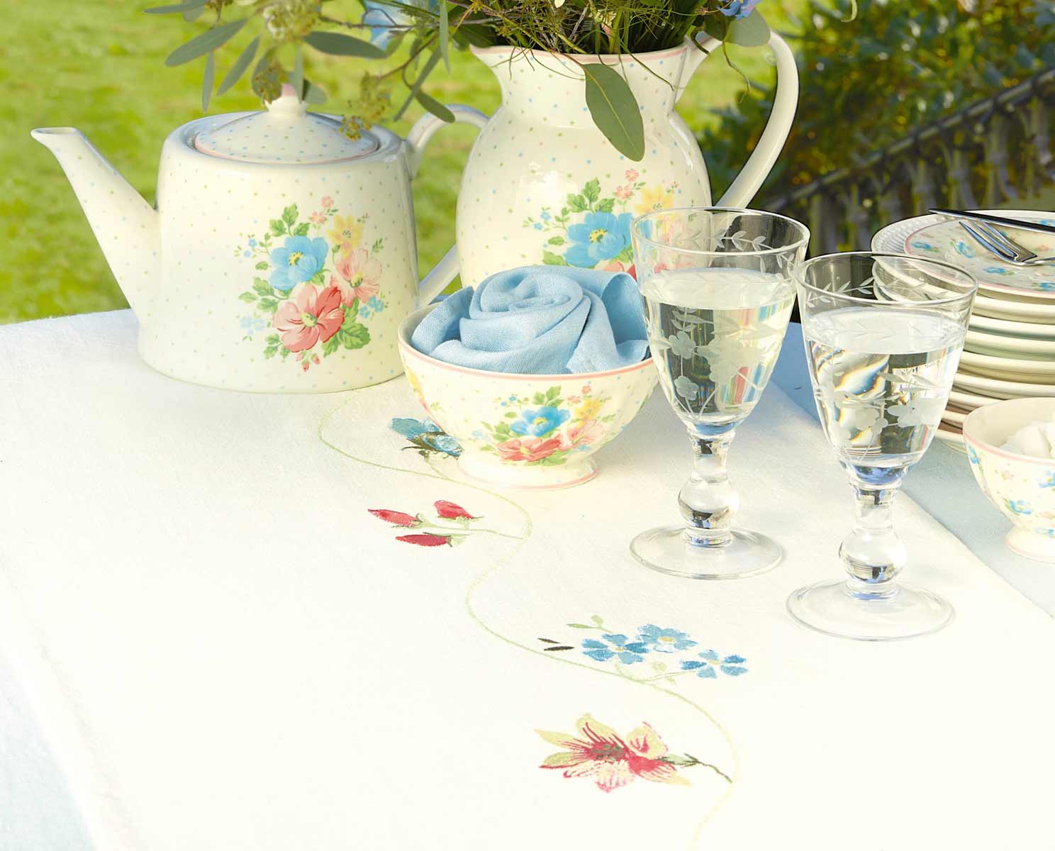 Ein Teeservice mit Blumen und Gläsern auf einem Tisch.