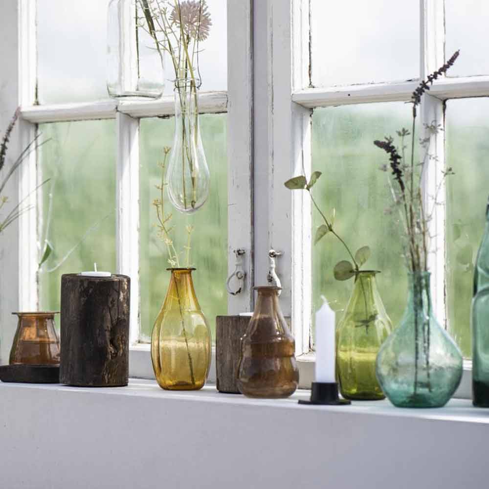 Ib Laursen UNIKA Holz-Teelichthalter zwischen farbigen Glasvasen auf einer hellen Fensterbank