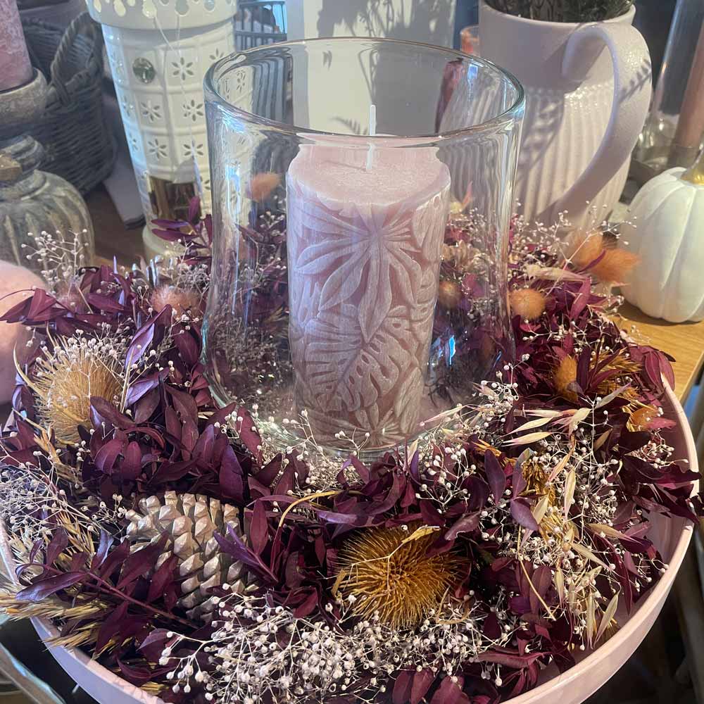 Die Alsaba Home - Deko Kranz Herbst zeigt eine rosafarbene Kerze in einem Glashalter, umgeben von getrockneten lila Blättern, Tannenzapfen und kleinen Blumen, arrangiert auf einem Holztisch.