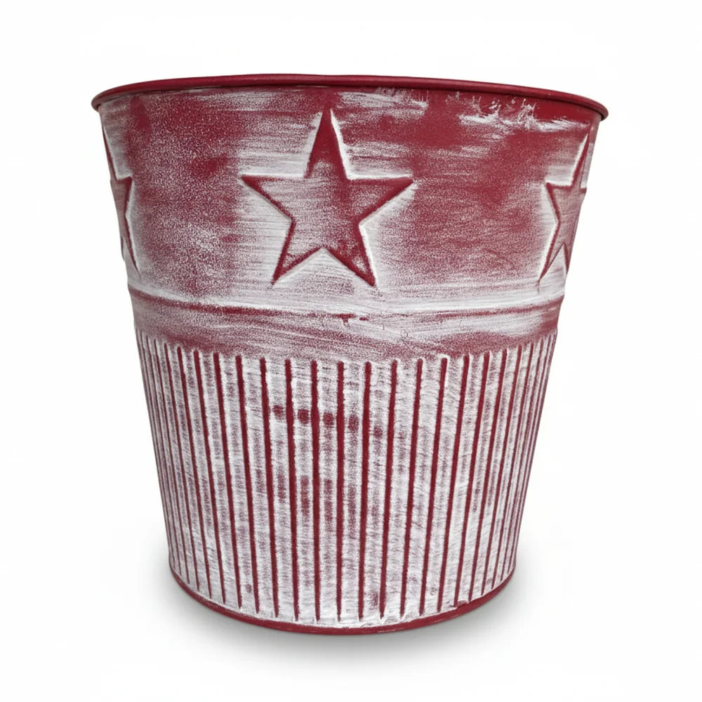 Der Alsaba Home - Metall Übertopf Weihnachten Rot ist ein roter Metalleimer mit geprägten Sternen und Streifen, der mit einer weiß getünchten Oberfläche versehen ist.