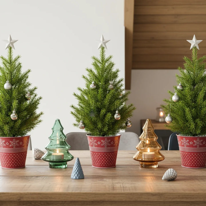 Drei Alsaba Home Metall Übertöpfe Weihnachten Rot mit je einem kleinen getöpferten Weihnachtsbaum mit silbernen Ornamenten und Sternspitzen stehen auf einem Holztisch zwischen Tannenzapfen und Kerzenhaltern in Form eines Weihnachtsbaums.