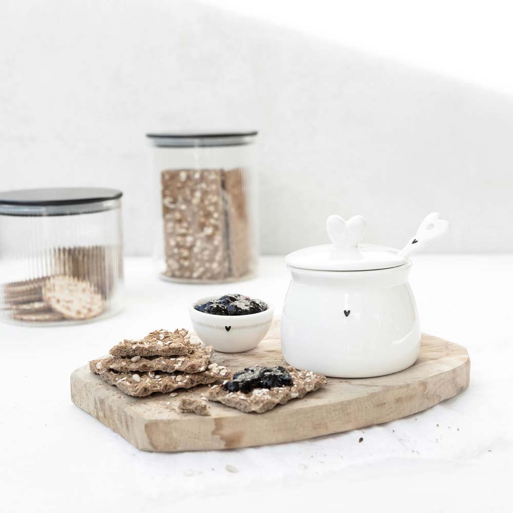 Bastion Collections - Marmeladendose mit Löffel Herz mit Herzmotiv und Schöpflöffel auf einem Holzbrett, dazu Cracker und eine kleine Schale Marmelade.