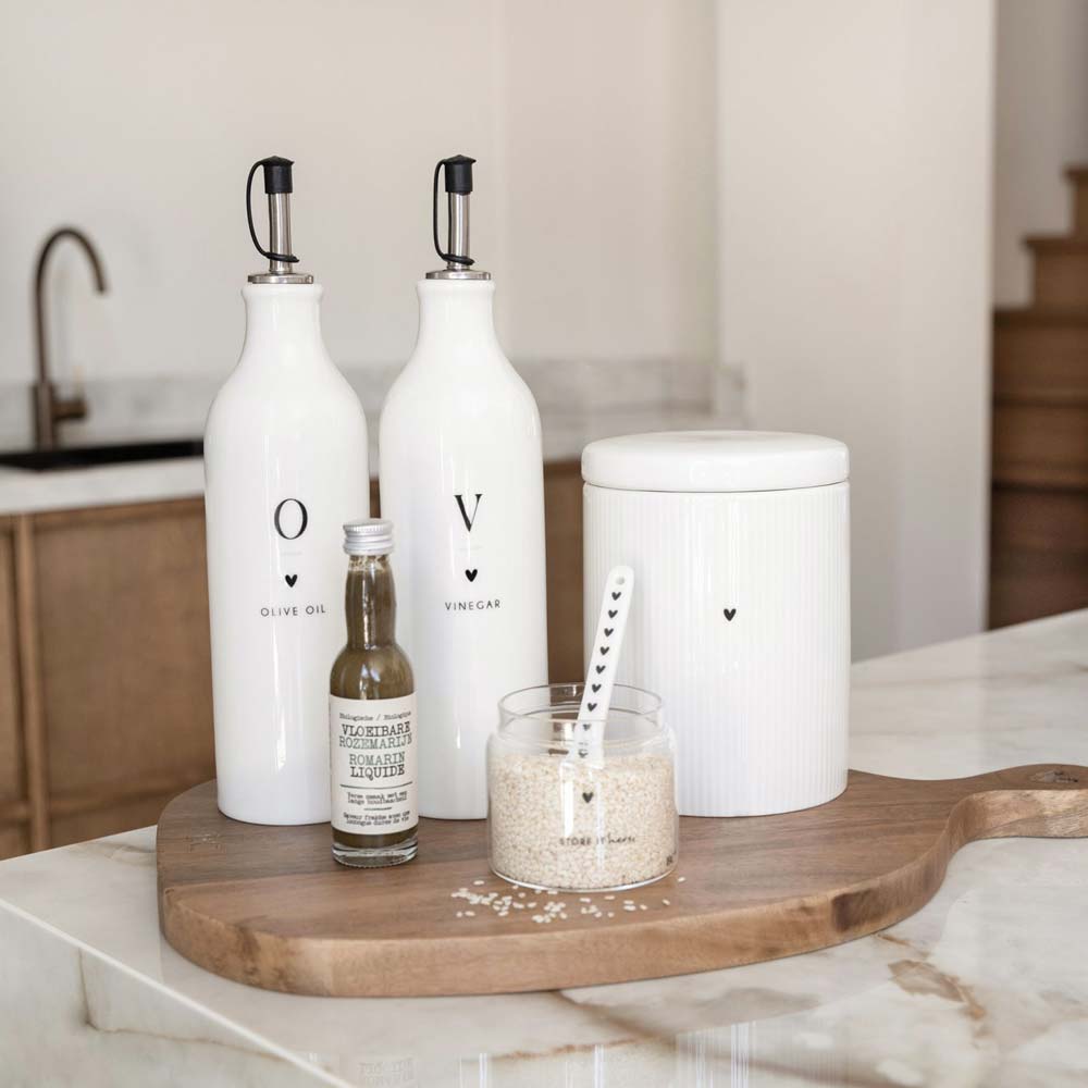 Eine Gruppe weißer Flaschen und eine Bastion Collections - Vorratsdose Herz Medium mit Rillen auf einem Schneidebrett.
