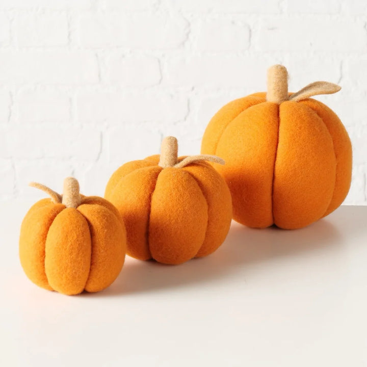 Das Boltze Dekokürbis Tikva Filz Orange 3er-Set besteht aus drei orangefarbenen Kürbisdekorationen aus Filz in verschiedenen Größen, die auf einer weißen Fläche mit weißem Backsteinmauerhintergrund präsentiert werden.