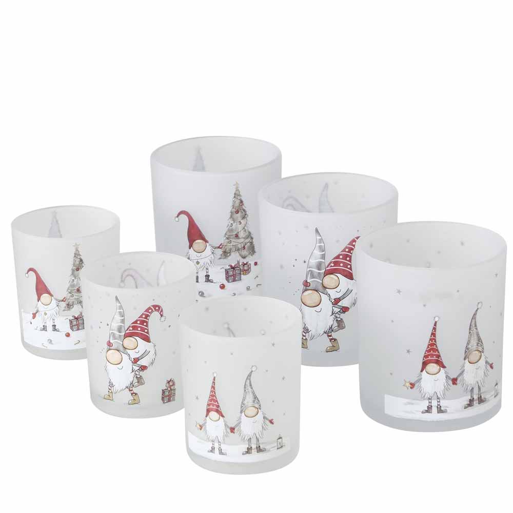 Sechs dekorative Kerzenständer aus dem Boltze - Windlicht Wichtel Bambi 2er-Set, geschmückt mit weihnachtlichen Wichtel-Motiven, mit roten und grauen Mützen, sowie kleinen Bäumchen und Geschenken.