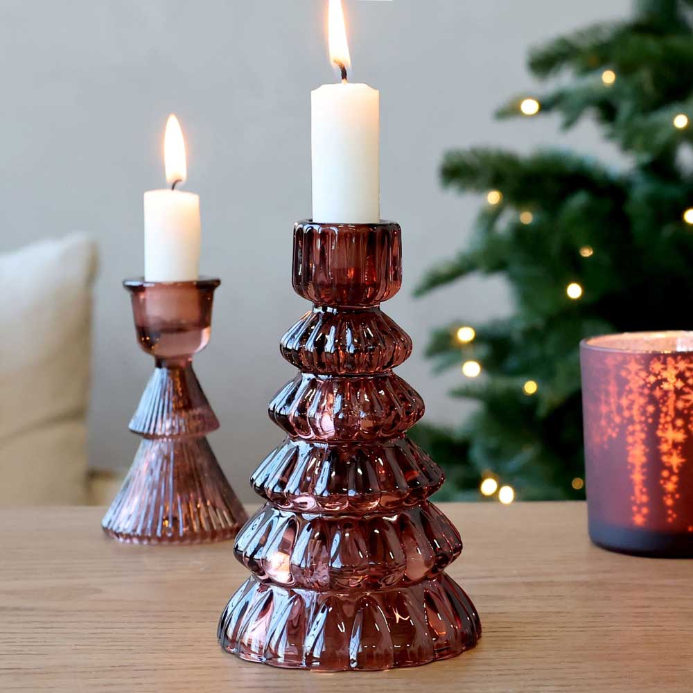 Auf einem Holztisch stehen zwei brennende Kerzen in Haltern mit der Aufschrift „Chic Antique – Kerzenständer Tannenbaum Cherry“, im Hintergrund sind ein verschwommener Weihnachtsbaum und sanft leuchtende Dekolichter zu sehen.