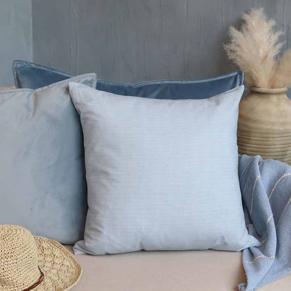 Der Chic Antique - Kissenbezug Maritimes Streifenmuster verleiht einem beigen Sofa einen hellblauen Streifen-Touch und wird mit zwei einfarbig blauen Kissen, einem Strohhut, einer blauen Decke und einer Vase aus Pampasgras im Hintergrund gestaltet.