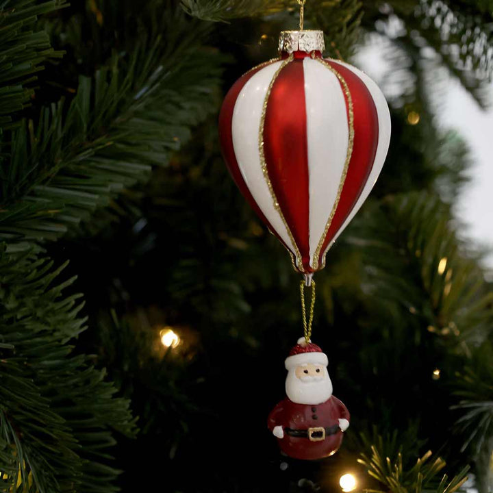 Ein Weihnachtsbaumschmuck in Form eines rot-weißen Heißluftballons mit einer darunter hängenden Miniatur-Weihnachtsmannfigur, bekannt als „Chic Antique – Luftballon mit Weihnachtsmann zum Aufhängen“.