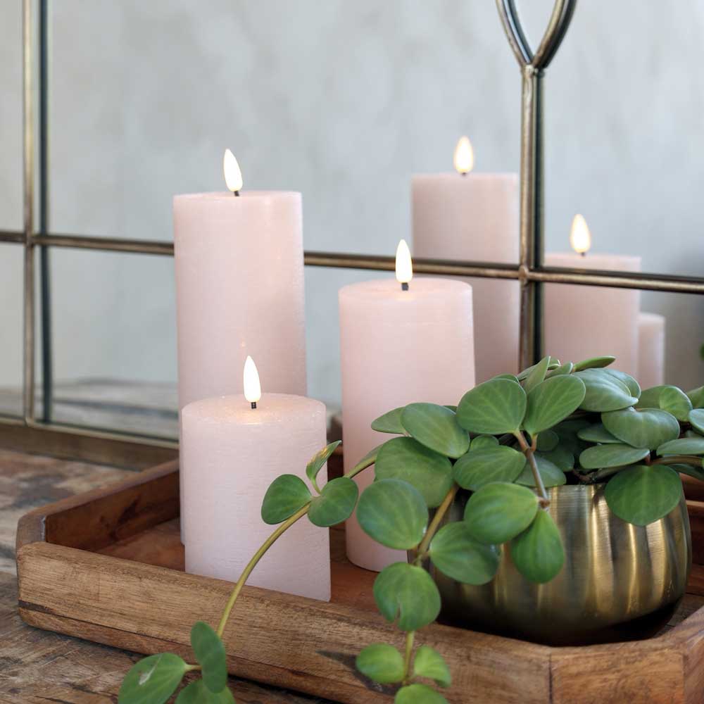 Auf einem Holztablett stehen drei brennende weiße Stumpenkerzen und eine Chic Antique - Fernbedienung für LED Kerze inkl. Batterie, platziert vor einem Spiegel mit Metallrahmen.