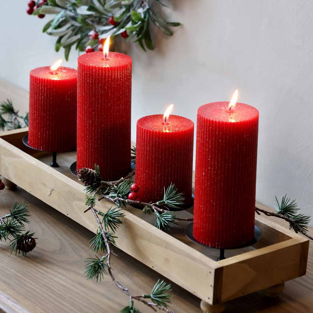 Vier Chic Antique – Stumpenkerzen mit Rillen und Glitzer in einem Holztablett, geschmückt mit Tannenzweigen und roten Beeren, auf einer Holzoberfläche.