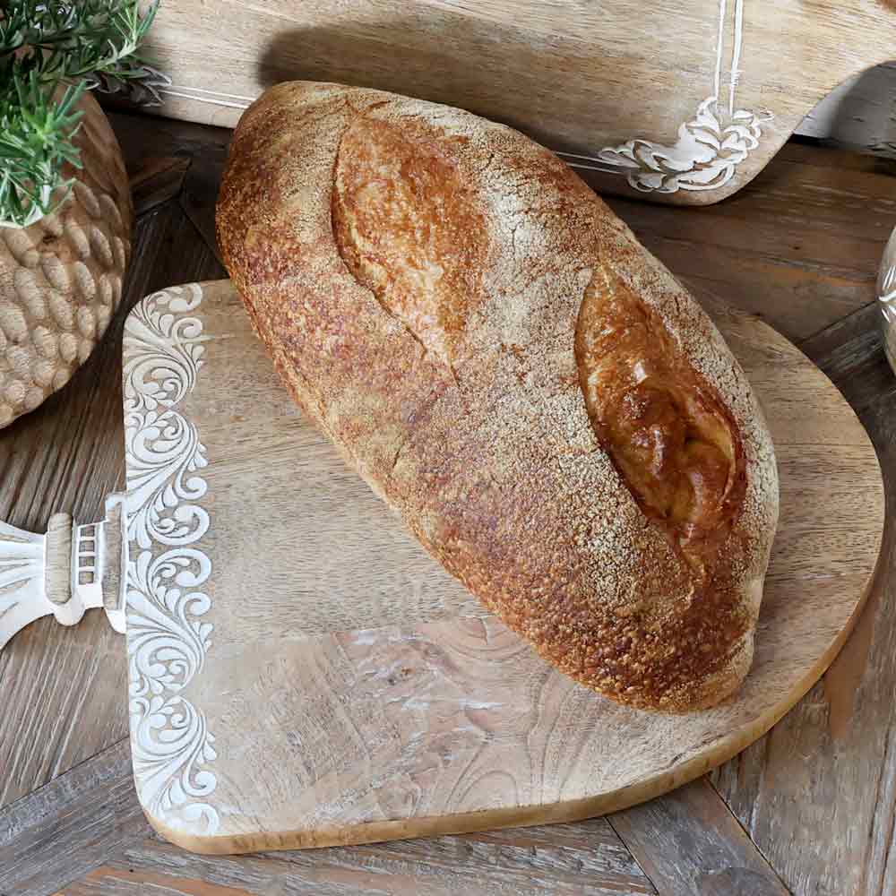 Ein Laib handwerklich hergestelltes Brot mit goldener Kruste ruht auf einem Chic Antique – Tapasbrett Tours mit Ornament.