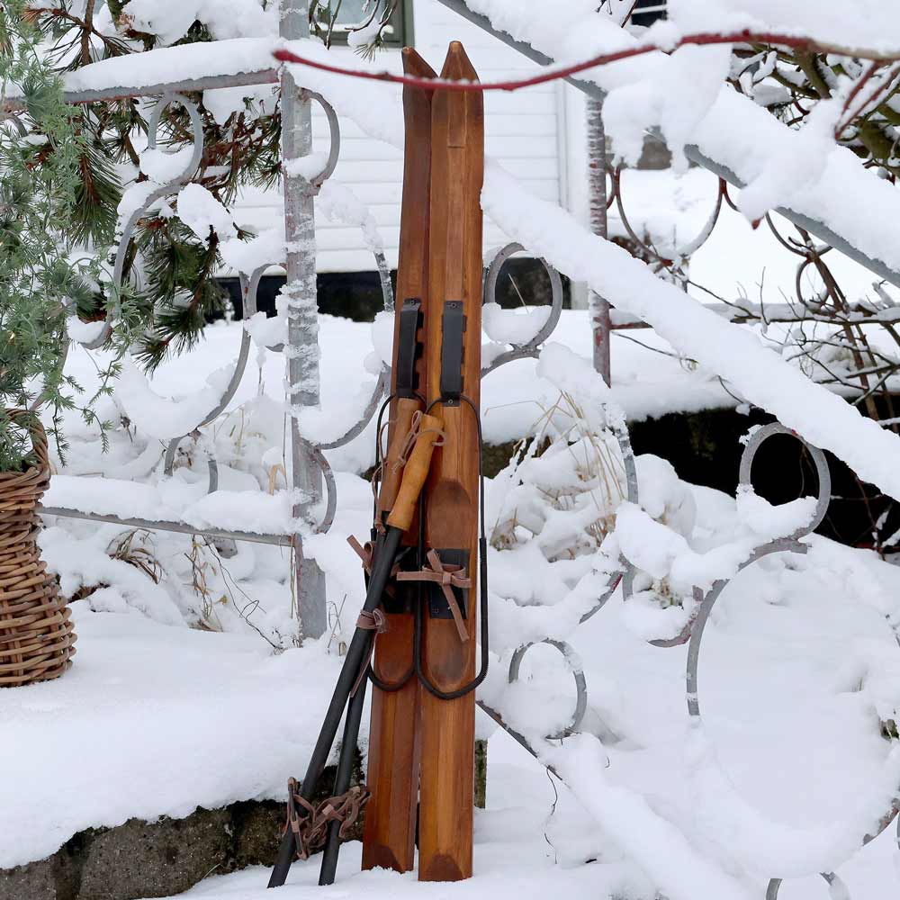 Die Chic Antique Vintage-Ski mit 90 cm langen Stöcken lehnen an einem schneebedeckten Geländer.