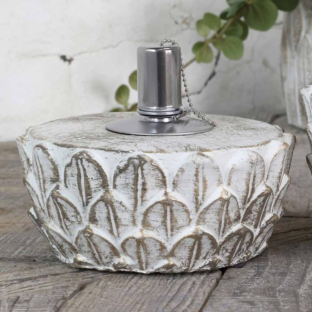 Eine verzierte, runde Öllampe mit einem grauen, gemusterten Keramiksockel und einem Dochthalter aus silbernem Metall steht auf einer Holzoberfläche, im Hintergrund sind grüne Blätter zu sehen. Chic Antique - Öllampe Zement mit Goldmuster