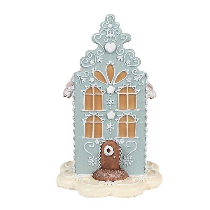 Das Clayre & Eef - Lebkuchenhaus 20 cm Blau Rosa ist ein dekoratives Lebkuchenhaus mit komplizierten weißen Zuckergussmustern, gelben Fenstern und einer braunen Tür, alles auf einem runden weißen Sockel.