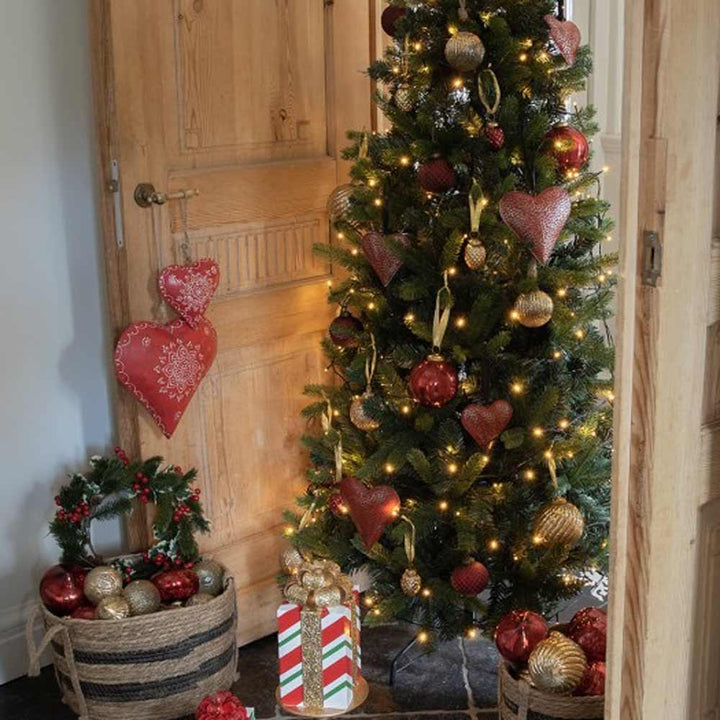 Ein geschmückter Weihnachtsbaum mit Lichtern, rot und gold marmorierten Ornamenten (Ø 7 cm) von Clayre & Eef, umgeben von Geschenktüten, Kränzen und einem roten herzförmigen Wandbehang.