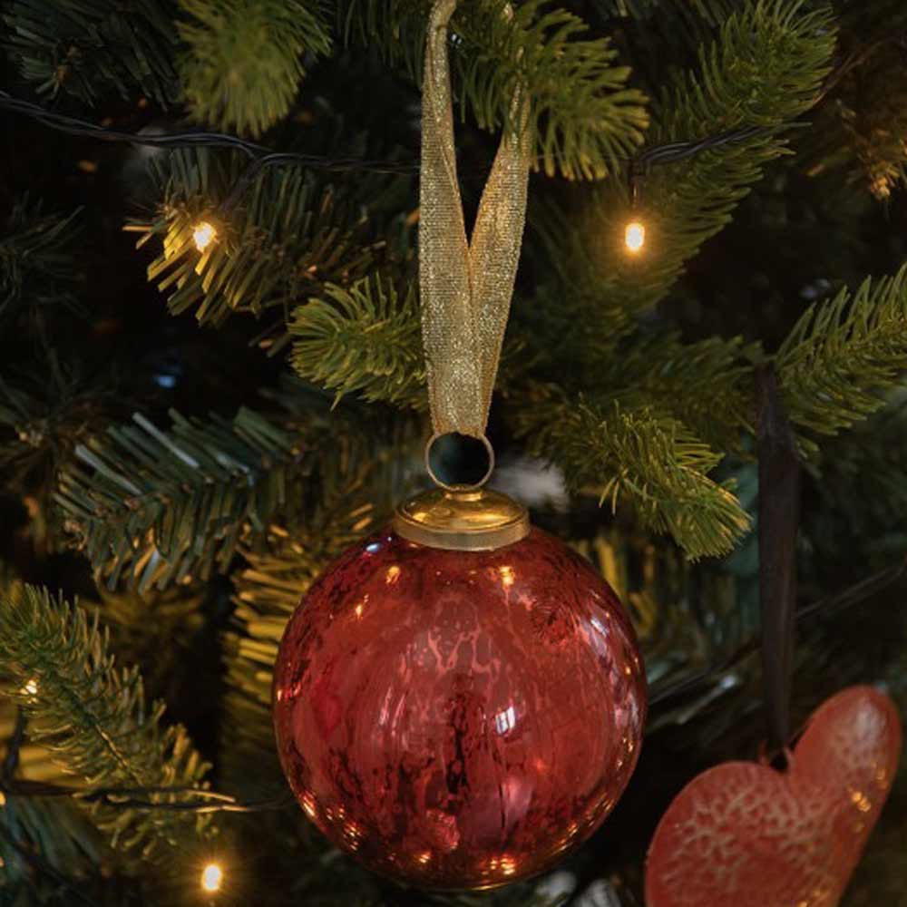 Eine Clayre & Eef - Weihnachtskugel Ø 7 cm Rot Marmoriert mit einer goldenen Schleife hängt an einem dekorierten immergrünen Baum mit Lichterkette.