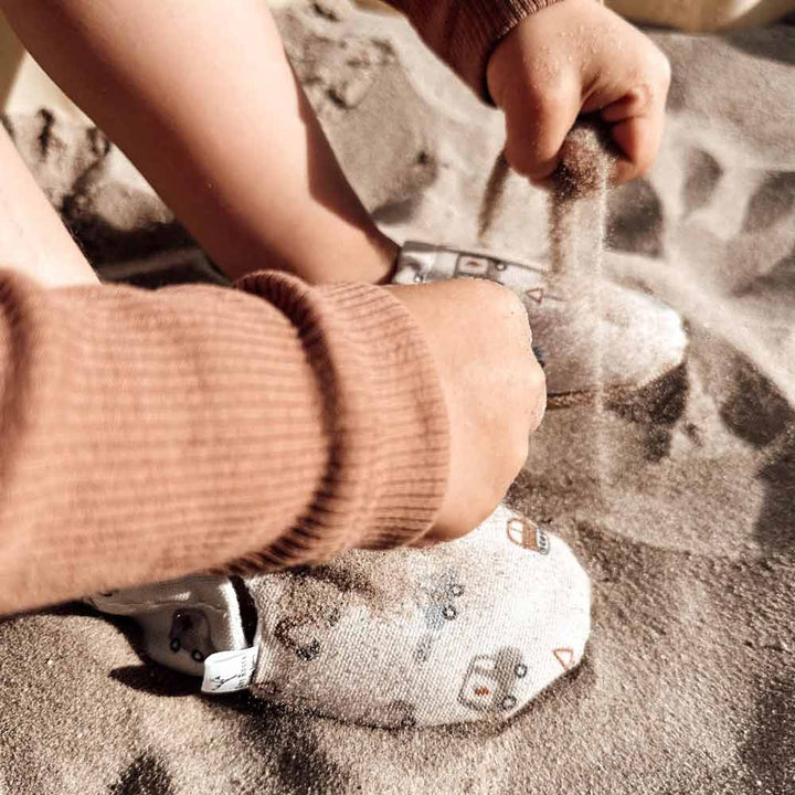 Kind spielt im Sand und trägt Cozy Roots - Lauflernschuhe Little Driver mit Tiermotiven.