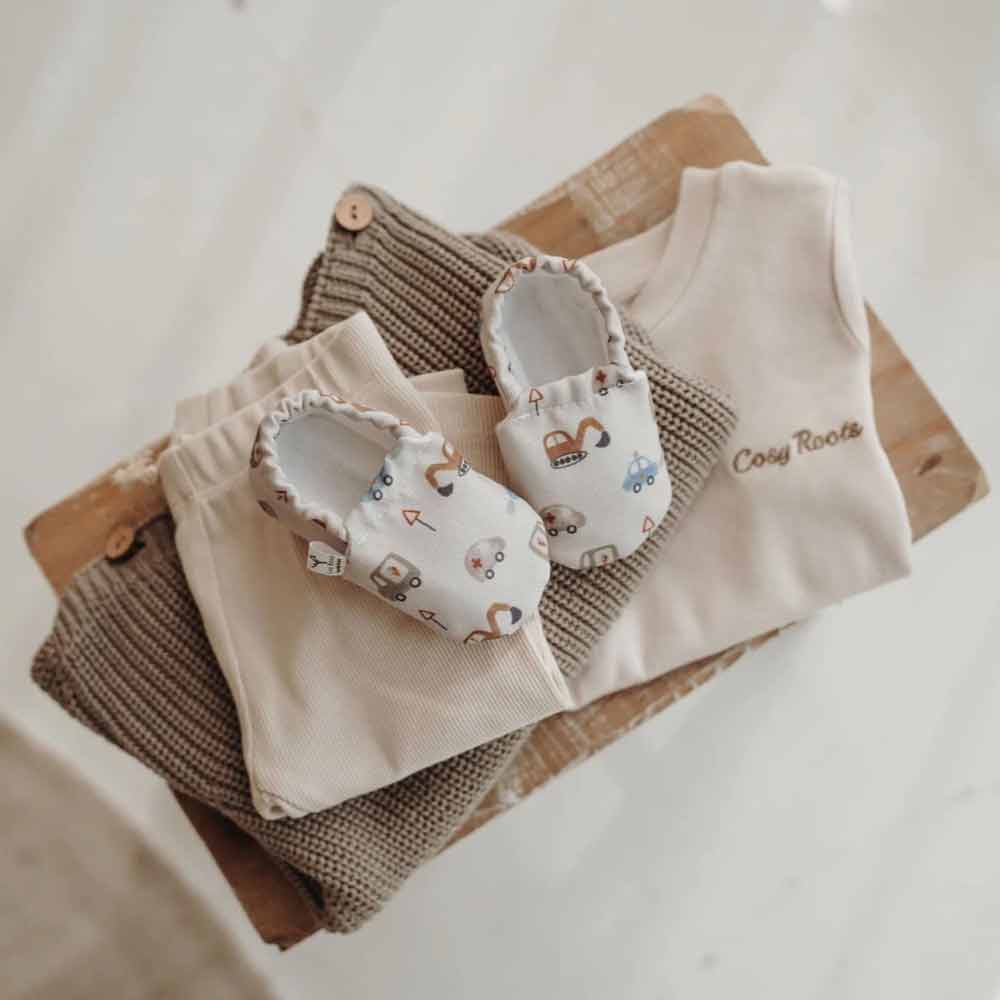 Ein Set aus Babykleidung und Cozy Roots – Lauflernschuhen Little Driver mit einer neutralen Farbpalette.
