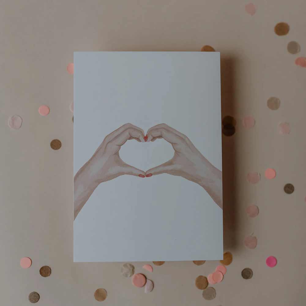 Die Eulenschnitt - Aquarellkarte Heart Hands zeigt zwei Hände, die auf einem beigen Hintergrund mit rosa und goldenem Konfetti ein Herz bilden.