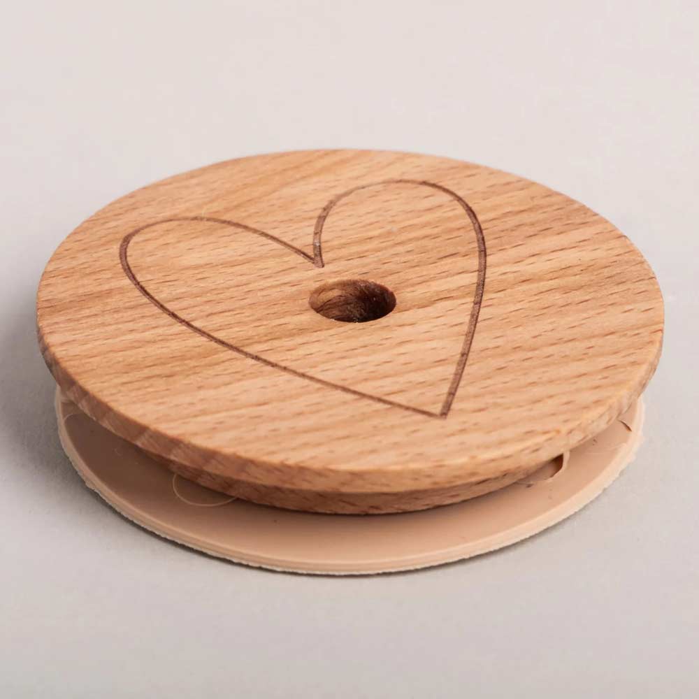 Der Eulenschnitt - Deckel Herz für Hohes Trinkglas ist ein runder Holzdeckel mit einer Herzgravur oben, einem zentralen Loch und einem beigen Kunststoffboden, der für hohe Trinkgläser geeignet ist.