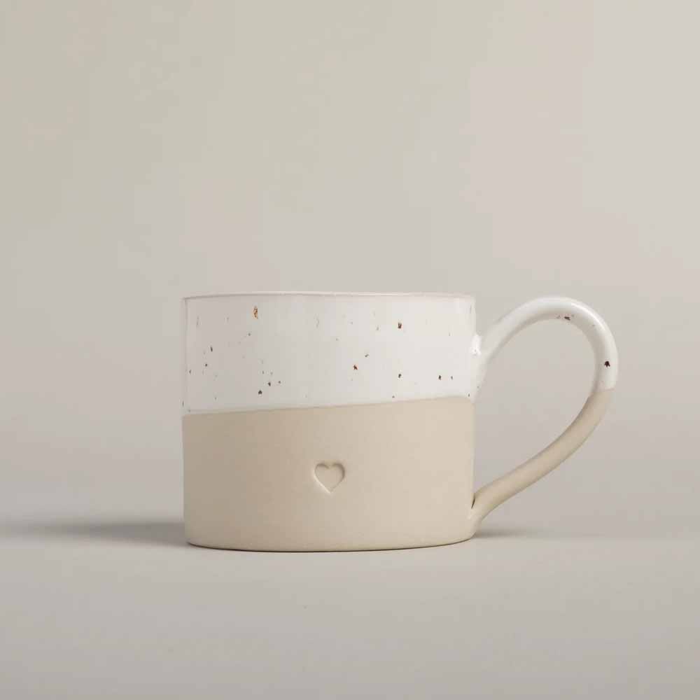 Eine Eulenschnitt - Tasse Herz im zweifarbigen Design in Weiß und Beige, mit einem kleinen Herzaufdruck auf dem beigen Teil in der Nähe des Henkels.