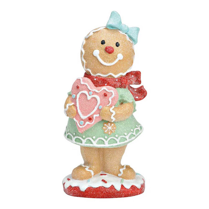 Das G. Wurm - Lebkuchenfrau-Bonbon zeigt eine Lebkuchenfigur in einem grünen Kleid, einem roten Schal und einer blauen Schleife, die einen rosa herzförmigen Keks hält.