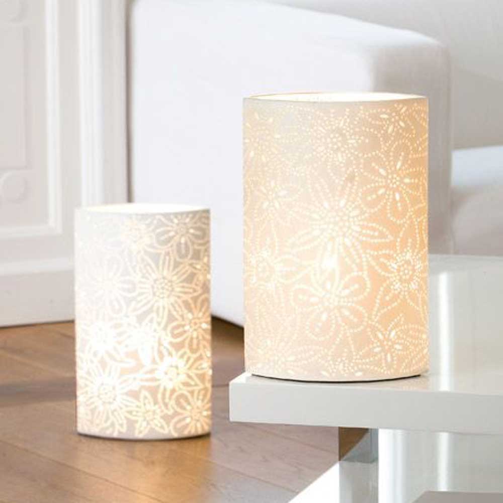 Zwei Lampen von Gilde - Lampe Porzellan Blumendesign mit aufwendigen Blumenmustern strahlen ein warmes Licht aus. Eine steht auf dem Boden, die andere elegant auf einem weißen Tisch und wertet das moderne Wohnzimmerambiente auf.