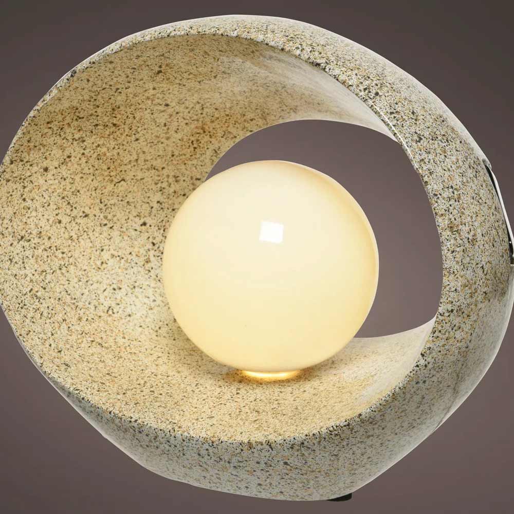 Die Gilde - Laterne Solar Ovalo, eine kugelförmige Solarlampe, leuchtet in einem gebogenen, strukturierten, steinähnlichen Gehäuse vor einem schlichten Hintergrund.