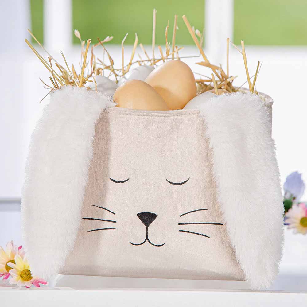 Die Gilde - Ostertasche Schlappi besteht aus einem Stoffkorb mit Hasengesicht und langen Ohren und ist mit hellbraunen Eiern und Stroh gefüllt.