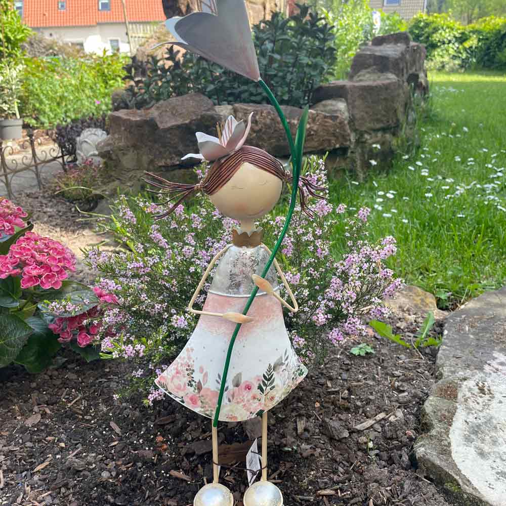 Ein Goldbach - Blumenmädchen mit Rosen steht inmitten von üppigem Grün und Blumen in einem Garten.