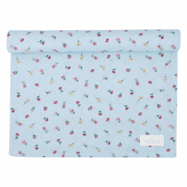Ein aufgerollter GreenGate - Lianca Tischläufer aus hellblauem Stoff zeigt kleine Blumenmuster in Rot, Rosa und Gelb und ist mit einem rechteckigen Etikett in der unteren rechten Ecke versehen.
