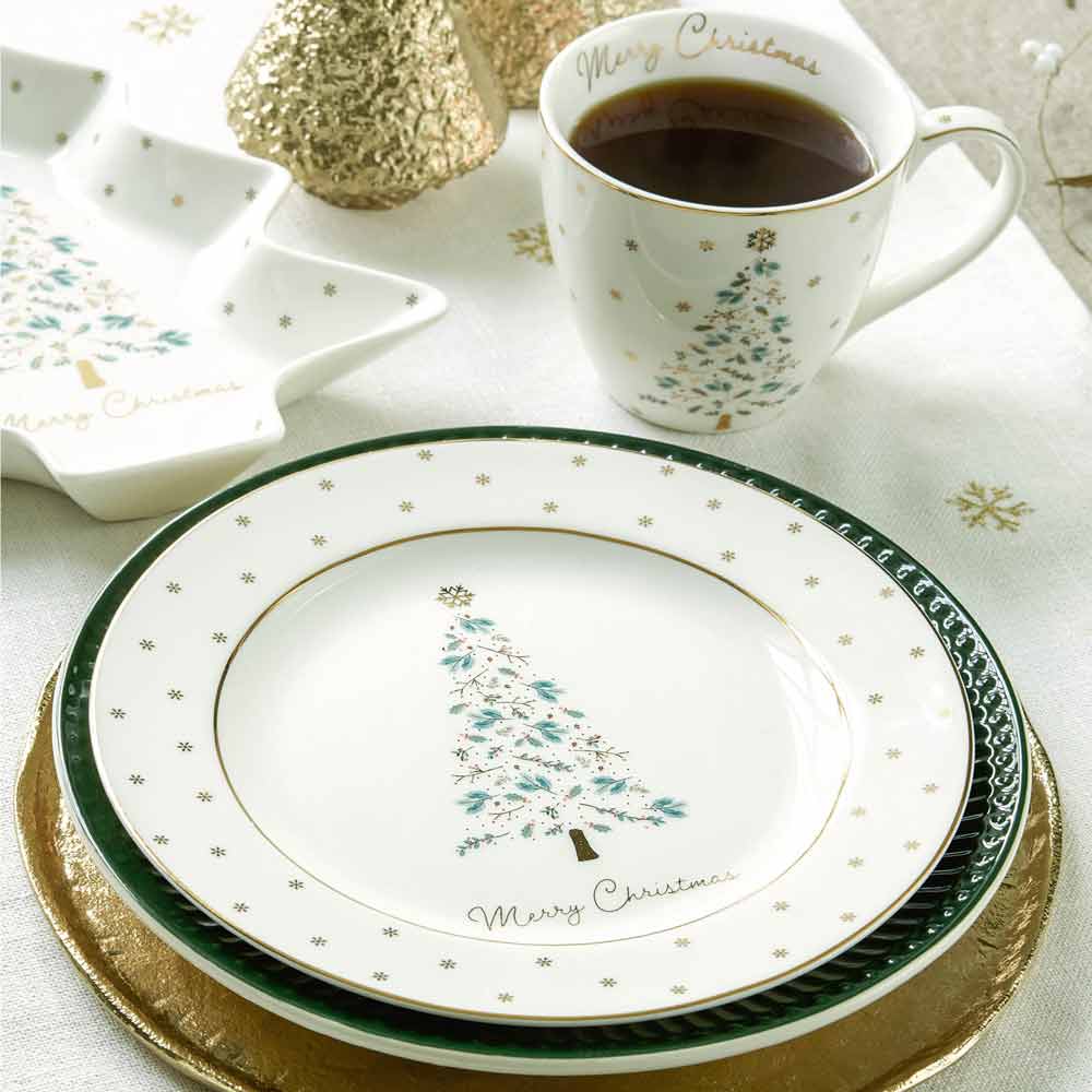 Eine weihnachtlich gedeckte Tafel mit Tellern im weißen GreenGate - Lucie Xmas Tannen Teller-Design, einer Kaffeetasse, einer sternförmigen Schale und dekorativen goldenen Gegenständen auf einer weißen Tischdecke.
