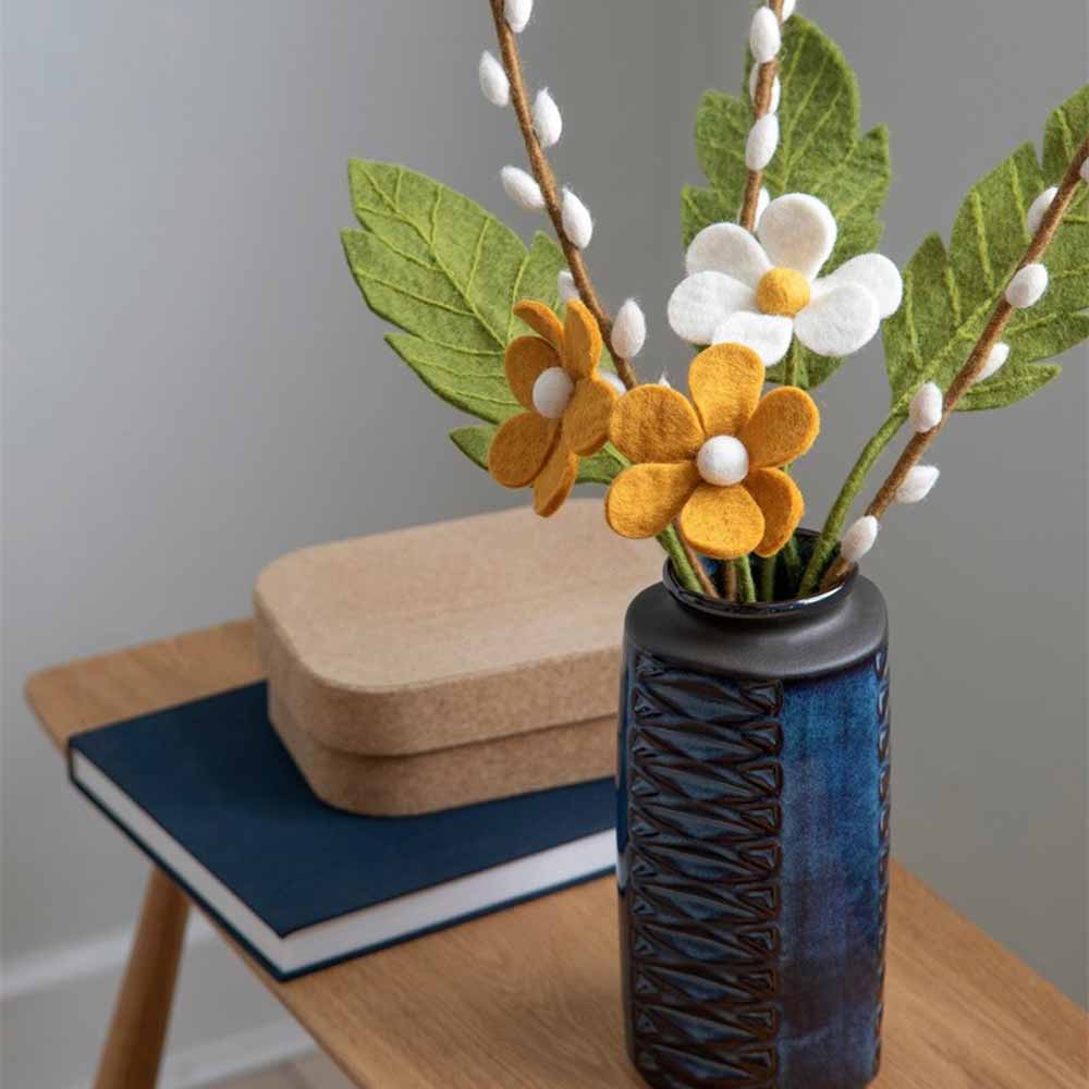 Satz mit Produktname: Gry & Sif – Anemone Filz in einer strukturierten Vase auf einem Holztisch mit Büchern.