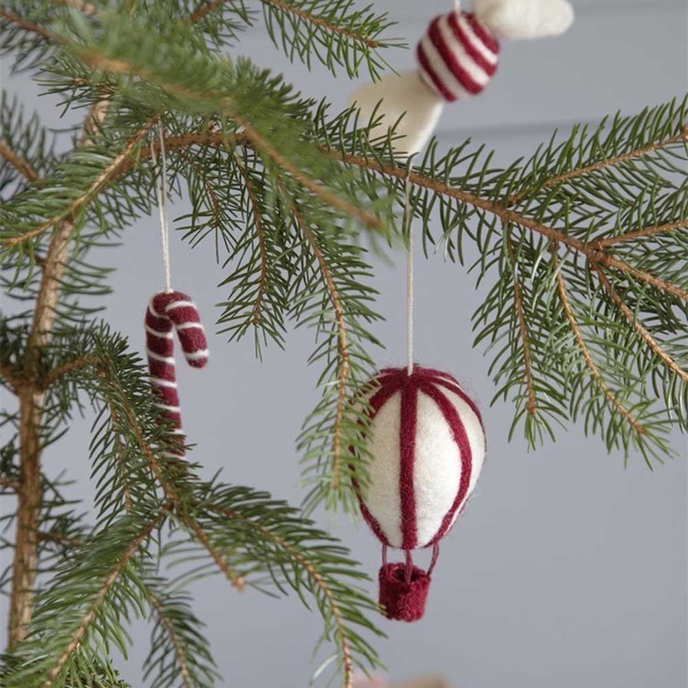 Das bezaubernde Gry & Sif Anhänger Balloon Vintage Filz-Ornament schmückt zusammen mit einer Zuckerstange die Zweige eines Tannenbaums.