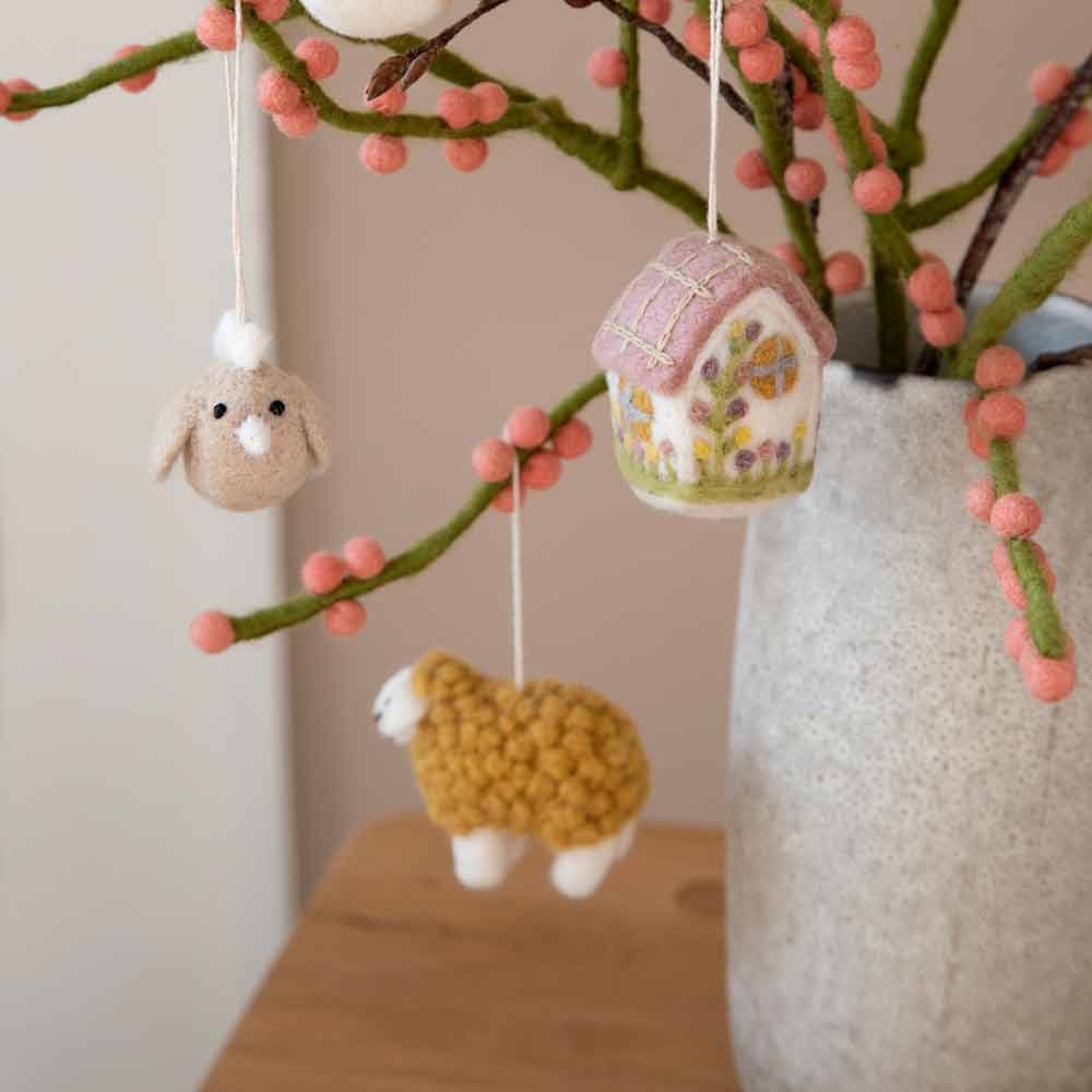 Eine Vase mit einem Gry & Sif - Anhänger Schaf Filz aus rosa Beeren und einem daran hängenden Schaf.